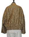 A gold sequined jacket with a high collar, shown from the back on a hanger with off-white trousers underneath, set against a plain light gray door.