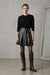 A black faux leather pleated mini skirt with a wide waistband and a small gold-tone zipper pull detail on the right side, shown against a plain white background.
