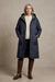 A long quilted hooded coat in dark navy blue with gold-tone snap buttons and black trim, hanging against a light gray background.