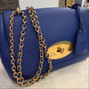 Blue handbag with a gold chain and clasp on a neutral background