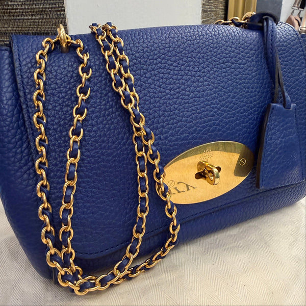 Blue handbag with a gold chain and clasp on a neutral background