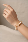 A strand of large, lustrous champagne-colored freshwater pearls arranged in a circle with a gold toggle clasp, photographed on a clean, solid off-white background.
