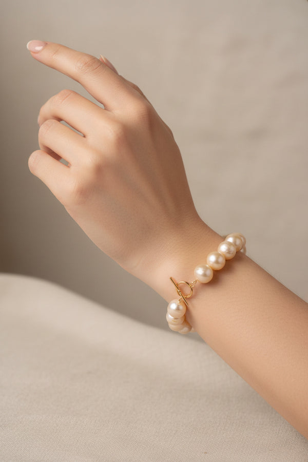 A strand of large, lustrous champagne-colored freshwater pearls arranged in a circle with a gold toggle clasp, photographed on a clean, solid off-white background.