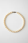 A strand of irregular white freshwater pearls with a small dark metal clasp, arranged in a circle on a textured gray background.