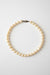 A strand of irregular white freshwater pearls with a small dark metal clasp, arranged in a circle on a textured gray background.