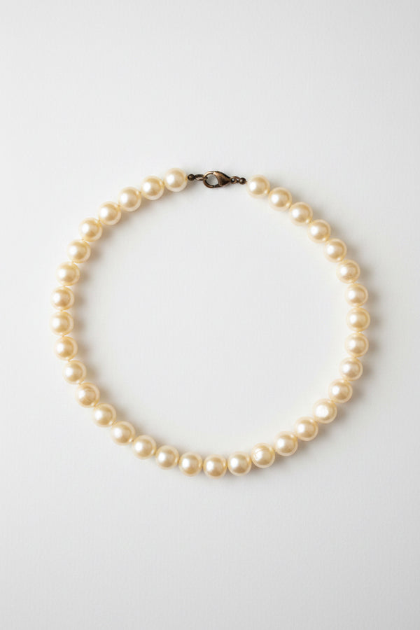 A strand of irregular white freshwater pearls with a small dark metal clasp, arranged in a circle on a textured gray background.