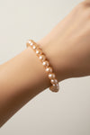 A strand of large, lustrous brownish-gold pearls arranged in a circle on a clean, off-white background.