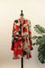 A long-sleeve shirt dress with an abstract geometric pattern in red, black, and beige, displayed on a dress form mannequin in front of a white door.