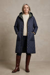 A long quilted hooded coat in dark navy blue with gold-tone snap buttons and black trim, hanging against a light gray background.