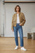 A cropped, long-sleeve tweed jacket in a textured brown and gold woven fabric, heavily embellished with scattered sequins, hanging on a wooden hanger against a plain white background.