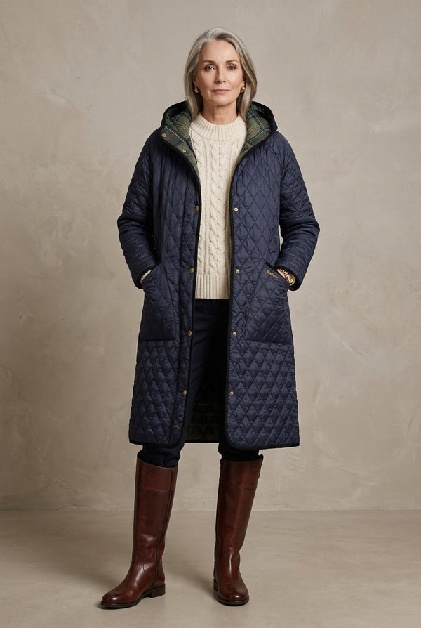 A long quilted hooded coat in dark navy blue with gold-tone snap buttons and black trim, hanging against a light gray background.